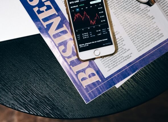 Smartphone displaying a declining stock chart placed on a Business magazine titled “The Future of Business,” with eyeglasses nearby—illustrating AI-driven data analytics shaping modern business strategy.