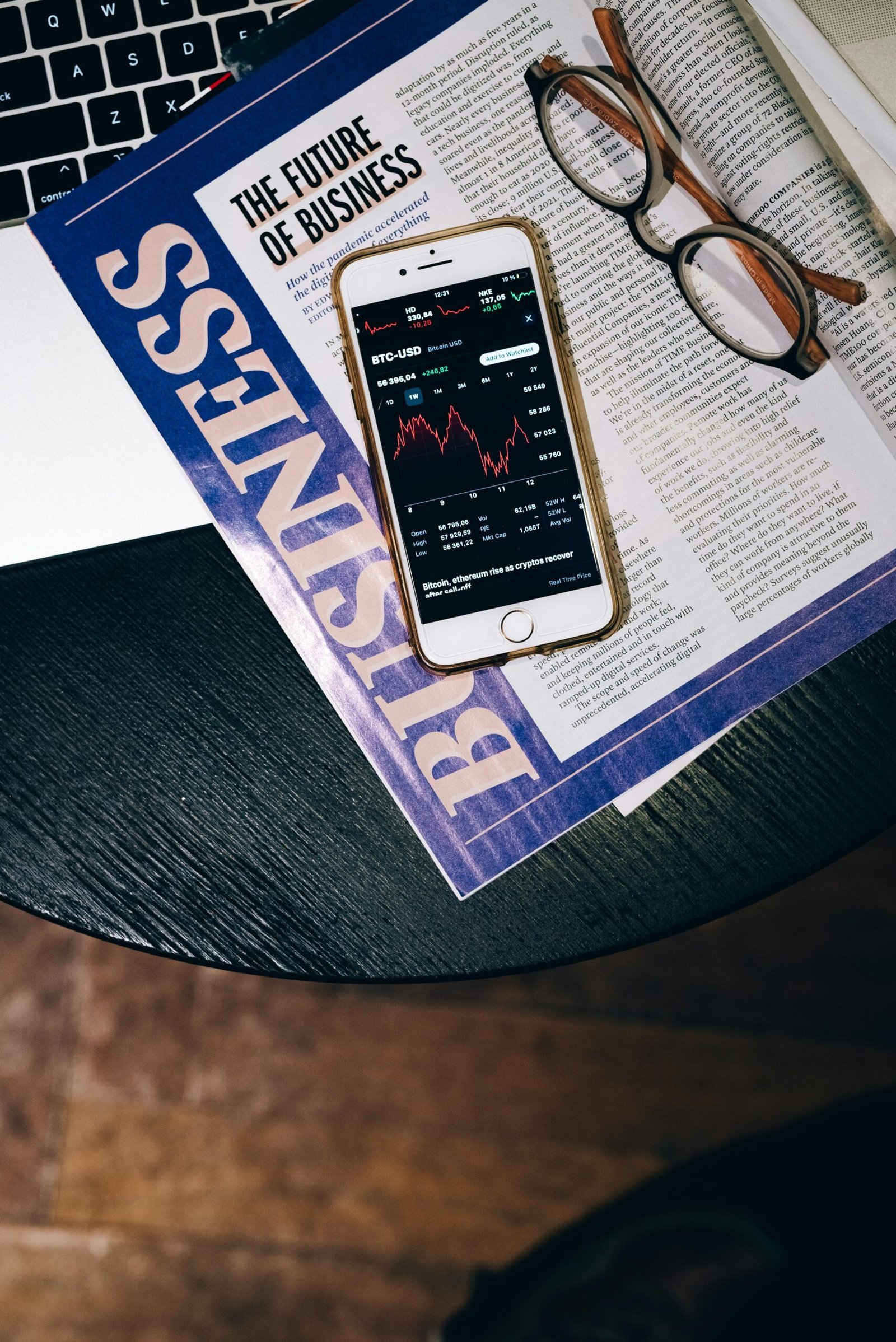 Smartphone displaying a declining stock chart placed on a Business magazine titled “The Future of Business,” with eyeglasses nearby—illustrating AI-driven data analytics shaping modern business strategy.