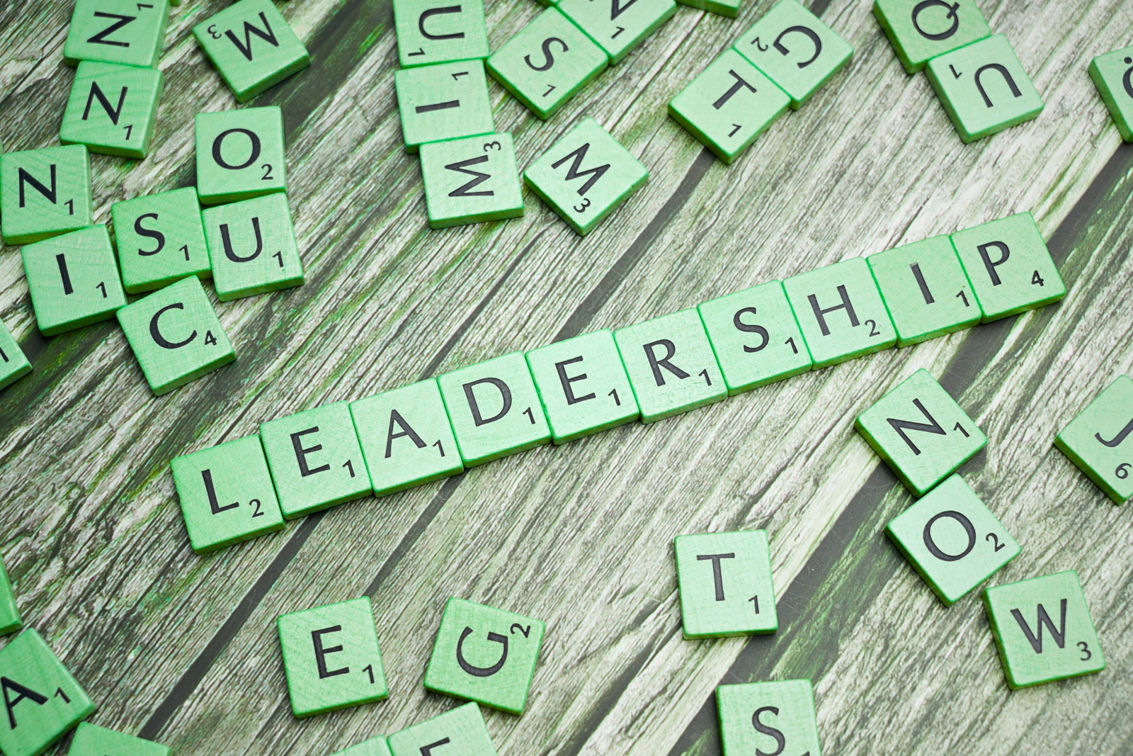 Green Scrabble-style letter tiles arranged on a wooden surface spell “LEADERSHIP,” surrounded by scattered letters, symbolizing evolving ideas and strategic thinking for leadership trends in 2026.
